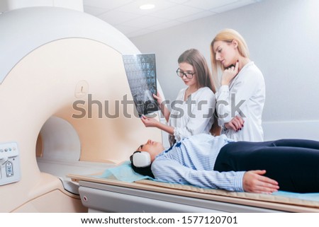 Two female models doctors examining patient and hold a picture in their hands after CT scan test