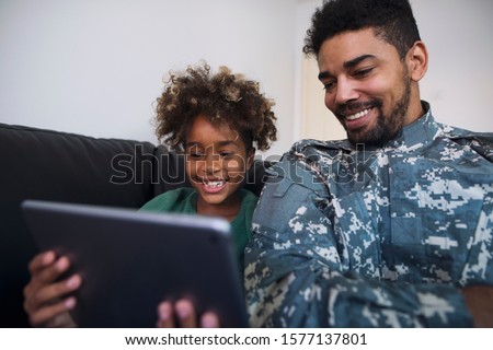 Father an off duty soldier being home with family enjoying and watching cartoons with his daughter on tablet computer.