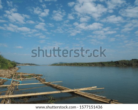 The picture of bamboo is tied into a large square by the river.  The background is a green mountain, white clouds and blue sky.