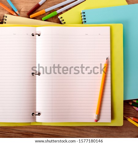 Student's desk with yellow project folder surrounded by various pens, pencils and notebooks.