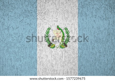 Guatemala flag depicted in bright paint colors on old relief plastering wall. Textured banner on rough background