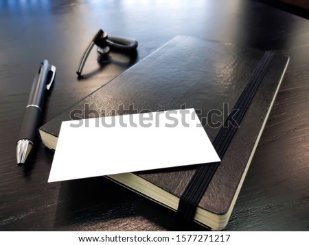 Blank white business card mock up template to put name and text on black wooden office work table with blurred laptop computer, mobile phone and notebook. Business finance workplace background.