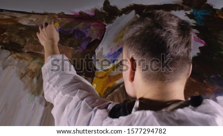 Artist designer draws an eagle on the wall. Craftsman decorator paints a picture with acrylic oil color. Painter painter dressed in a paint coat. Indoor. Dark magic cinematic look.
