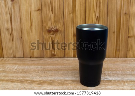 Black colour stainless steel tumbler or cold and hot storage cup on wooden background.