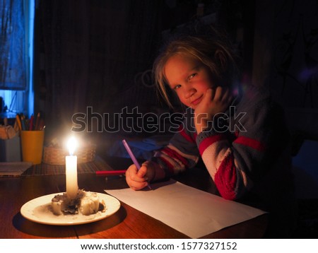 little girl draws by candlelight. The absence of electricity, the living conditions of the child