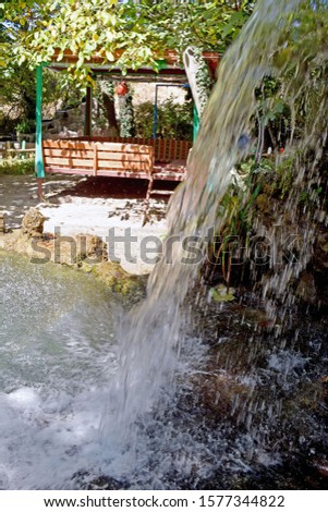 A close up of a waterfall in a Restaurant with the water cascading down and splashing into a pond creating lots of bubbles and the restaurant seating area in the background