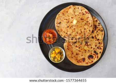Indian Food - Aloo Paratha or Indian Potato stuffed Flatbread. Served with butter, pickle and masala potatoes. over light background with copy space. Royalty-Free Stock Photo #1577364655