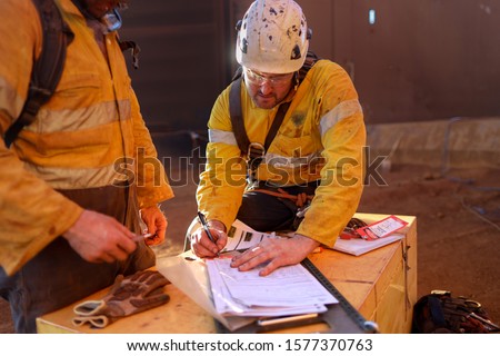 Miners wearing a white fall protection safety helmet signing name, signature in from safety control permit to work isolation lock box prior to work on opening field construction mine site Australia 