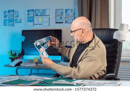 A man in glasses develops the design of a mobile application. Choose a color scheme for the user interface. Using templates and palettes in the designer's work. The execution of the order.