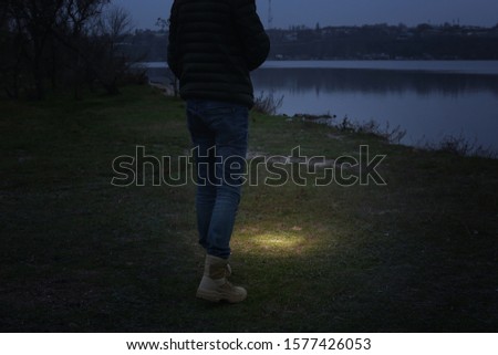 Man with flashlight walking near river, closeup
