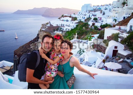 Happy  family on vacation in the greek islands of Santorini. Mom, dad and daughter with positive emotions are photographed against the sunset and the city of Oia, Santorini. Family Vacation a