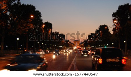 Champs Elysées avenue in Paris by night with the blurred cars in foreground and the Arc de Triomphe in the distance with the street lighting on and the dark trees and buildings aside