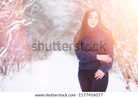 A young girl in a winter park on a walk. Christmas holidays in the winter forest. Girl enjoys winter in the park.
