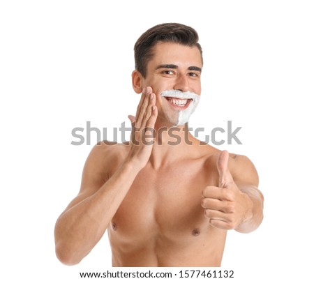 Handsome young man with shaving foam on his face showing thumb-up against white background