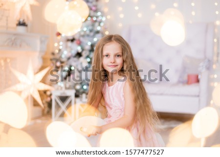 a girl with long blond hair makes a wish, dreams on the background of a Christmas tree. In the hands of gift. Christmas lights