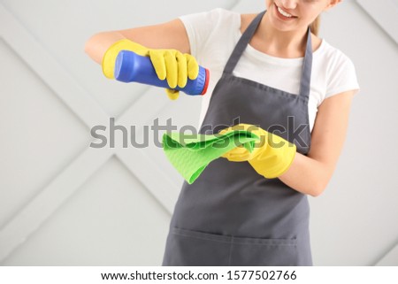 Female janitor with cleaning supplies on grey background