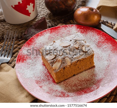 Gluten free dessert pastry food shot of an autumn almond brownie on a red plate covered in snow sugar and coffee mug on a warm table set. Christmas breakfast sweets for celiacs and food intolerants.