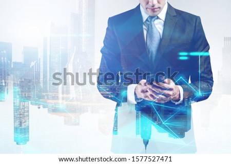 Unrecognizable young businessman looking at smartphone in modern city with double exposure of blurry network hologram. Concept of internet connection and communication. Toned image