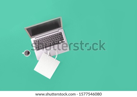 Laptop with gift shopping bag on trending green background with coffee cup. Online internet shopping concept flat lay with copy space. Black Friday Cyber Monday