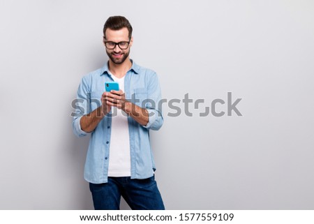Photo of attractive macho guy perfect appearance neat hairstyle easy-going person holding browsing telephone wear specs casual denim outfit isolated grey color background Royalty-Free Stock Photo #1577559109