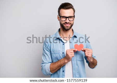 Photo of attractive handsome guy holding little red paper heart overjoyed symbolizing cardiology healthcare wear specs casual denim outfit isolated grey color background