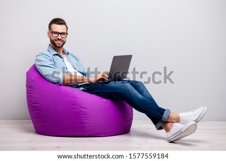 Full body profile photo of funny guy holding notebook browsing chatting colleagues sitting comfy soft armchair wear specs casual denim outfit isolated grey color background Royalty-Free Stock Photo #1577559184