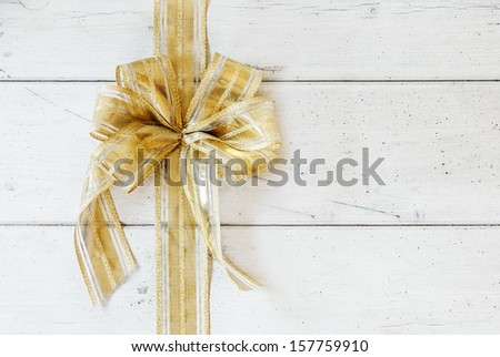 Shiny metallic ornamental golden bow for celebrating Christmas, anniversary, Valentines or a birthday on a white painted background of wooden boards with copyspace