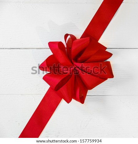 Romantic vivid red Christmas or Valentines bow placed diagonally across white painted boards as a festive background for your greeting or wishes