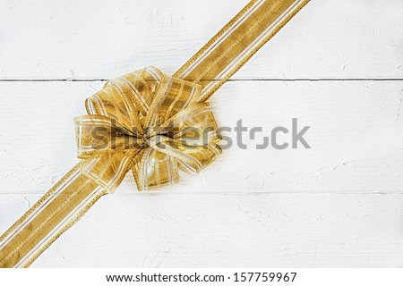 Decorative gold Christmas bow arranged diagonally on white painted boards with copyspace for your seasonal greeting