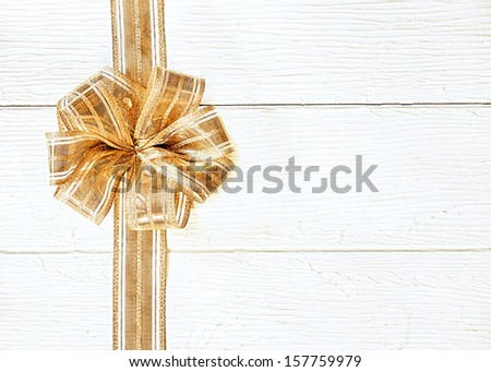 Beautiful gold Christmas ribbon and decorative bow forming a side border on a background of textured white painted wood with copyspace