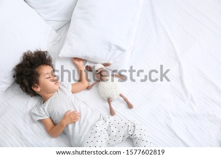Little African-American girl with toy sleeping in bed Royalty-Free Stock Photo #1577602819