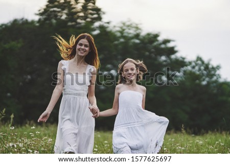A woman in a white dress holds the hand of a little daughter on the nature in the mountains