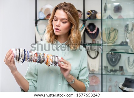Successful young saleswoman demonstrating colorful bracelets from different precious stones in jewelry shop Royalty-Free Stock Photo #1577653249