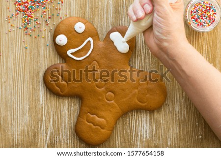 Baked gingerbread cookie man decorated with icing by woman hand on the wooden background