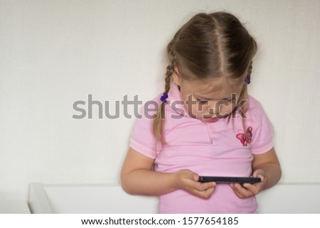 Caucasian child of three age holding mobile phone and looking on it on the white background