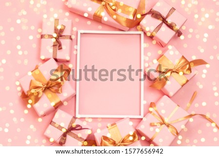 Christmas decorative composition frame with paper pink present boxes, gold bow and confetti on grey background. Flat lay, top view for holiday shopping on boxing day