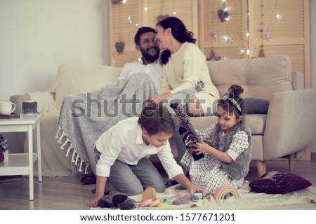 little boy girl having fun, friendship between siblings, family leisure time in living room. Children sister and brother playing drawing together on floor while young parents relaxing at home on sofa