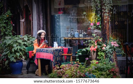 A happy Asian woman sits outside a bar in the old town, camera in hand, with travel ideas