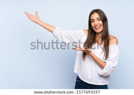 Young woman over isolated blue background extending hands to the side for inviting to come
