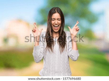Young hispanic brunette woman with fingers crossing at outdoors