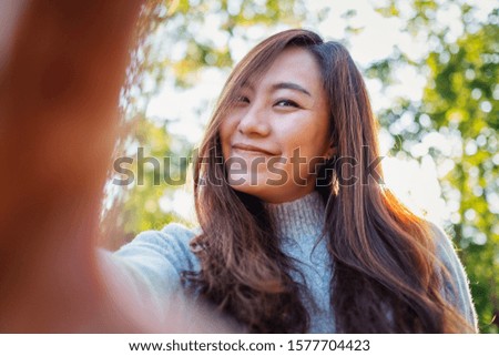 Portrait image of a happy beautiful asian woman making selfie photo in park