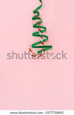 Striped cane, gift wrapping ribbon swirling Christmas tree on pink pastel color background. Funny minimal fashion composition. Happy holiday creativity flat lay layout. New year preparations concept
