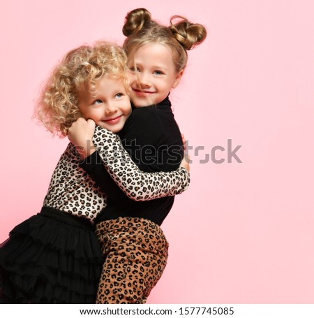 Two happy nice kids girls best friends sisters in leopard print clothes pants and sweater are hugging smiling feeling love on pink background