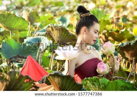 Asian woman is holding pink lotus in lotus filed with sunlight on the morning with Thai dress