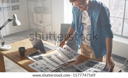 Creative Designer Works on a Storyboard, Looks at His Sketches and Concepts, Choosing the Best Drawings for His Project. Video Editing, Comics Compilation, Application UI or Game Plot. High Angle Royalty-Free Stock Photo #1577747569
