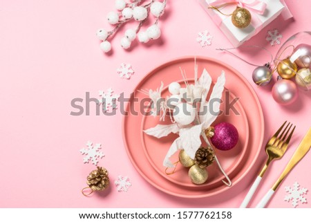 Christmas table setting with white plate and white pink and golden decorations on pink background. Top view copy space.