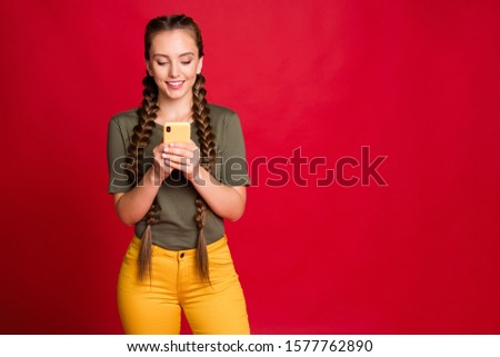 Photo of pretty lady long braids holding telephone hands reading new positive comments interested wear casual yellow trousers green t-shirt isolated red color background