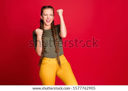 Photo of funny lady long braids raising fists up celebrating best winning football team amazing day wear casual green t-shirt yellow trousers isolated red color background