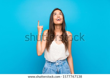 Young woman over isolated blue background pointing up and surprised