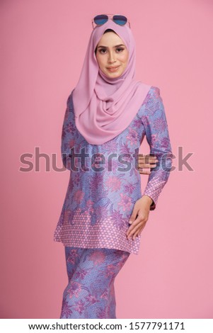 Beautiful female model wearing light purple batik design "baju kurung" with hijab, a modern lifestyle outfit  for Muslim woman isolated over pink background. Eidul fitri fashion and beauty concept.